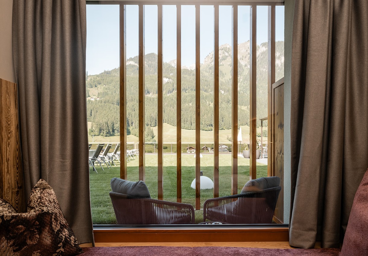 Blick aus einem Fenster auf eine Wiese mit Liegestühlen und Bergen im Hintergrund