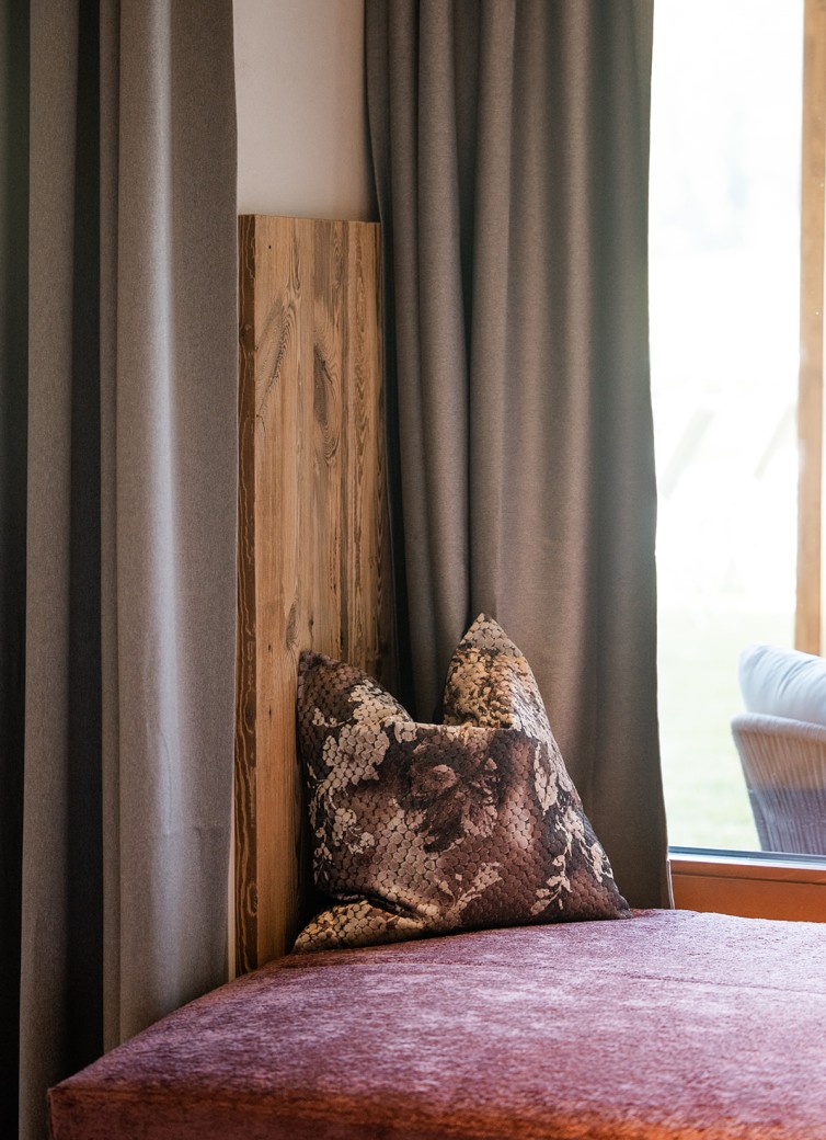 Holzbank mit braunem Kissen vor grauen Vorhängen und Fenster