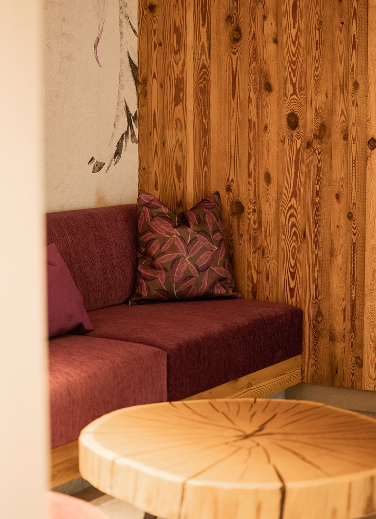 Lila Sofa mit gemustertem Kissen, Holzwand und runder Holztisch