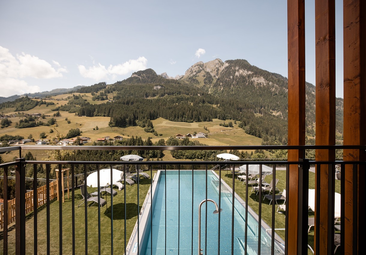 Blick auf einen Pool mit Berglandschaft im Hintergrund, Sonnenschirme und Liegen