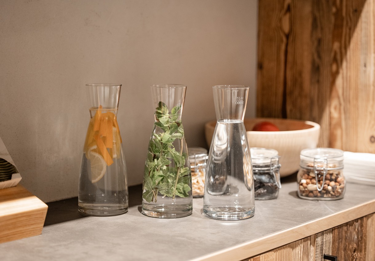 Drei Glaskaraffen mit Wasser, Zitrusfrüchten, Kräutern und verschiedenen Nüssen auf der Theke