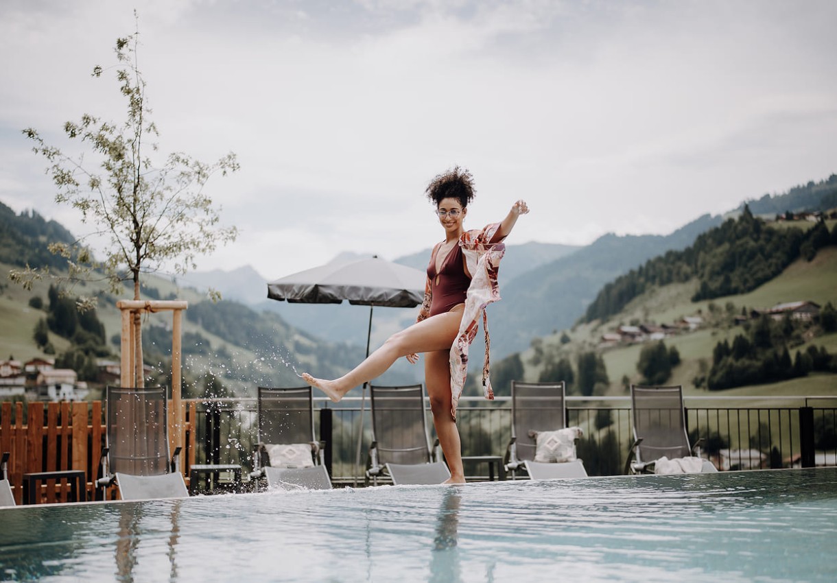 Frau genießt Infinity-Pool vor einer Berglandschaft