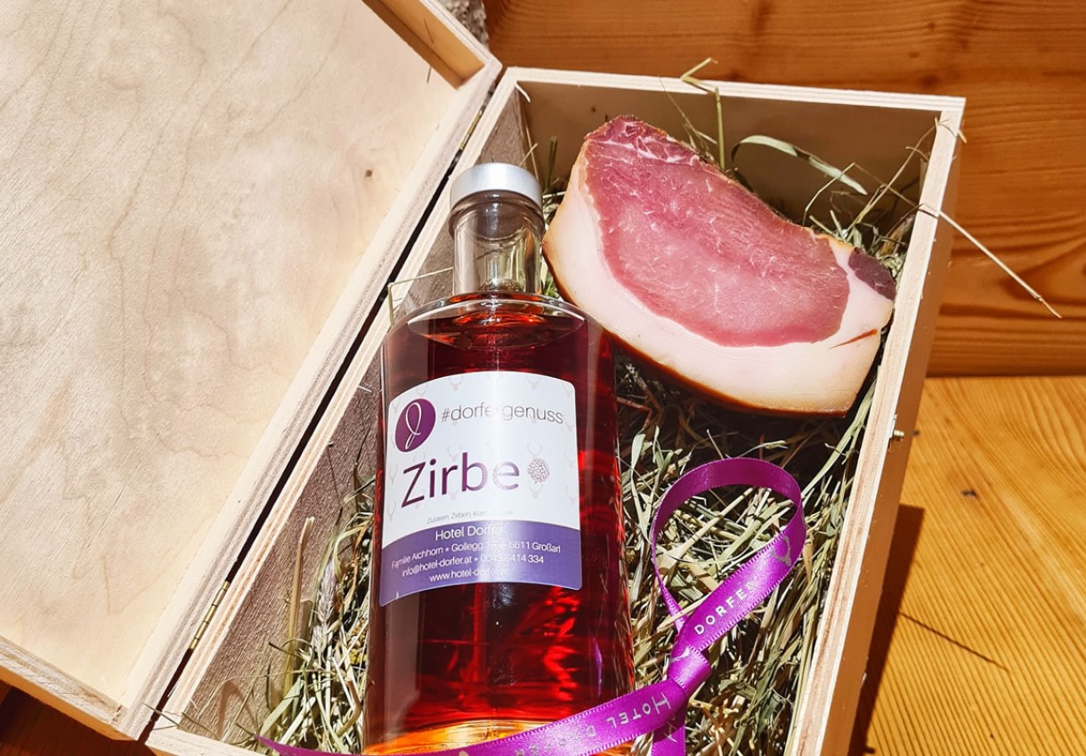 Flasche Zirbenschnaps und Schinken in Holzkiste auf Stroh