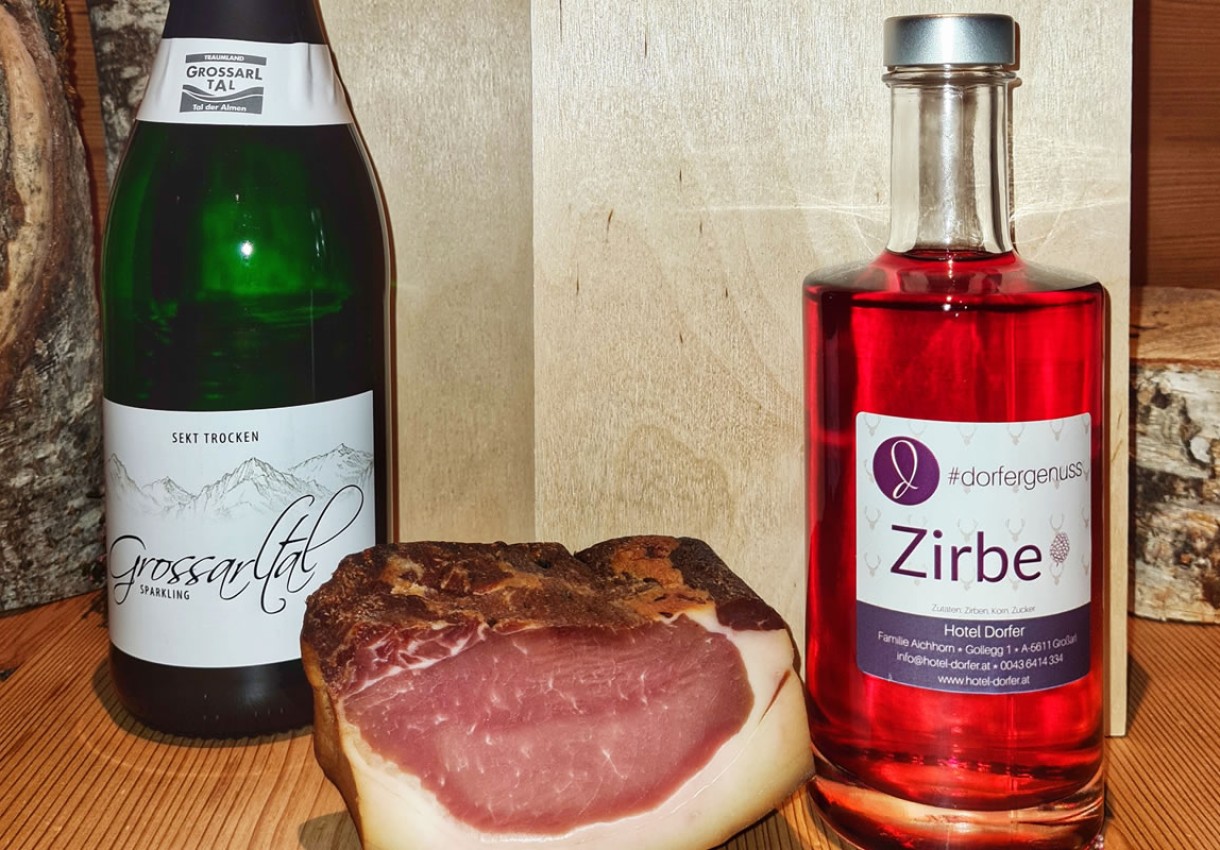 Eine Flasche Sekt, Zirbenlikör und ein Stück Speck auf Holzhintergrund