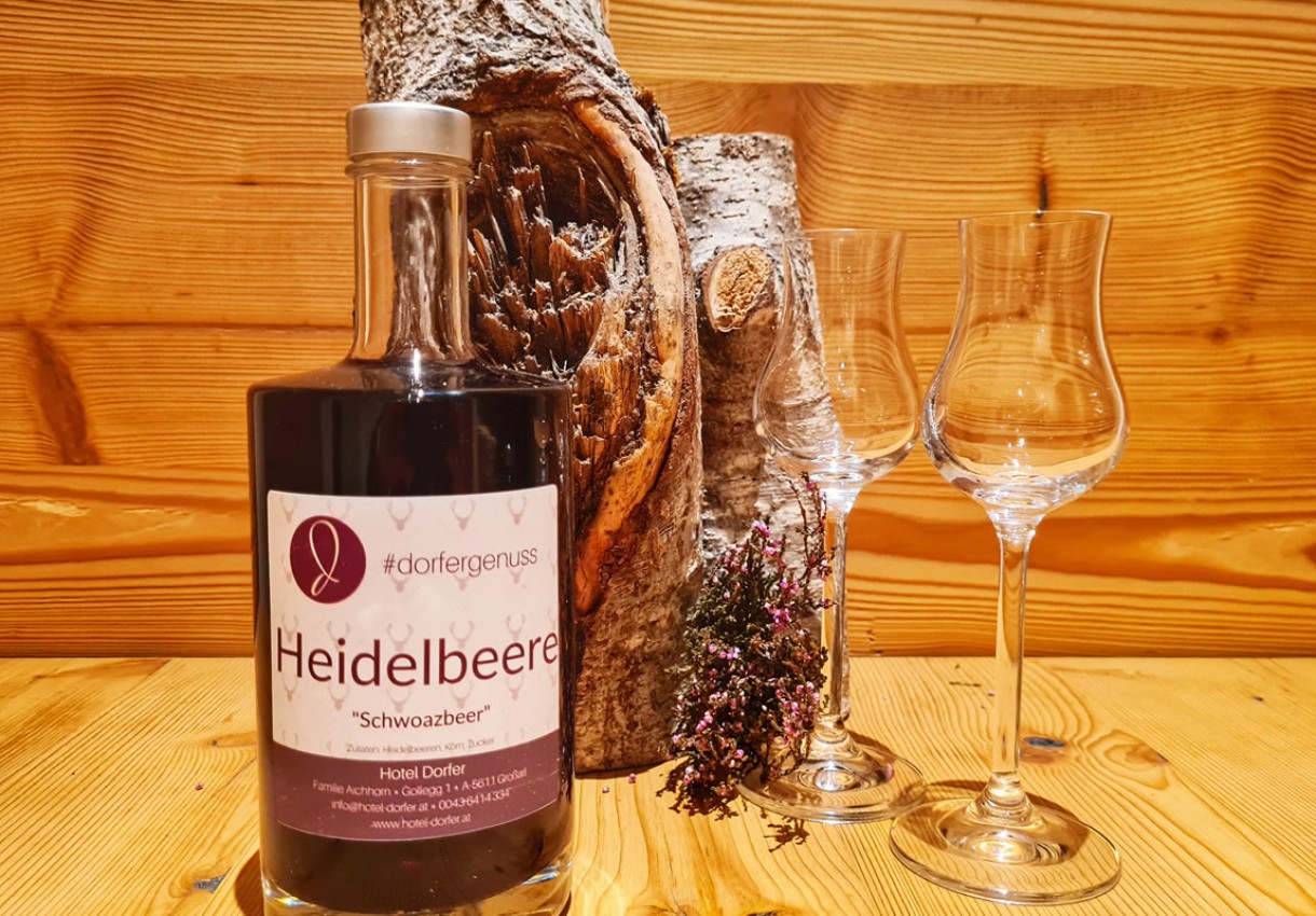 Flasche Heidelbeerlikör und zwei Gläser vor Holzdekor und Heidekraut