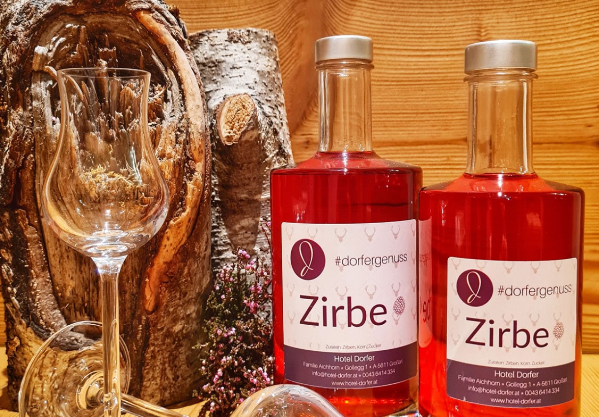 Zwei Flaschen roter Zirbenlikör mit Weinglas vor rustikalem Hintergrund