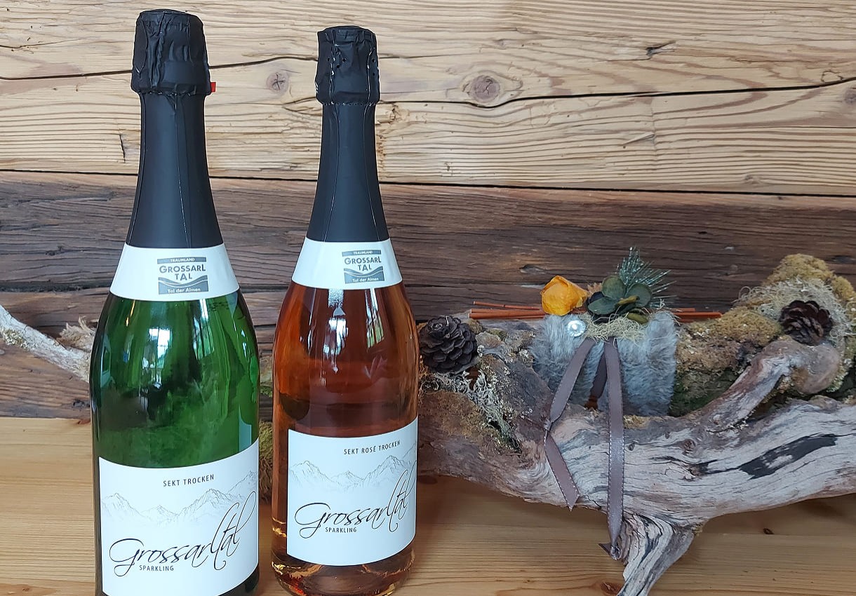 Zwei Flaschen Sekt stehen auf einem Holztisch neben einer dekorativen Holzskulptur