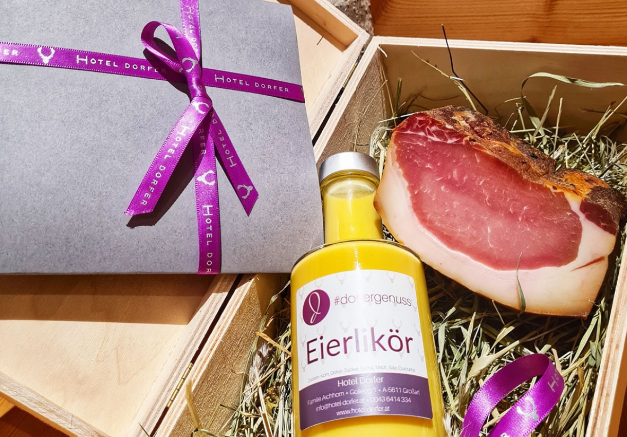 Flasche Eierlikör neben einem Stück Schinken in einer Holzkiste mit lila Schleife