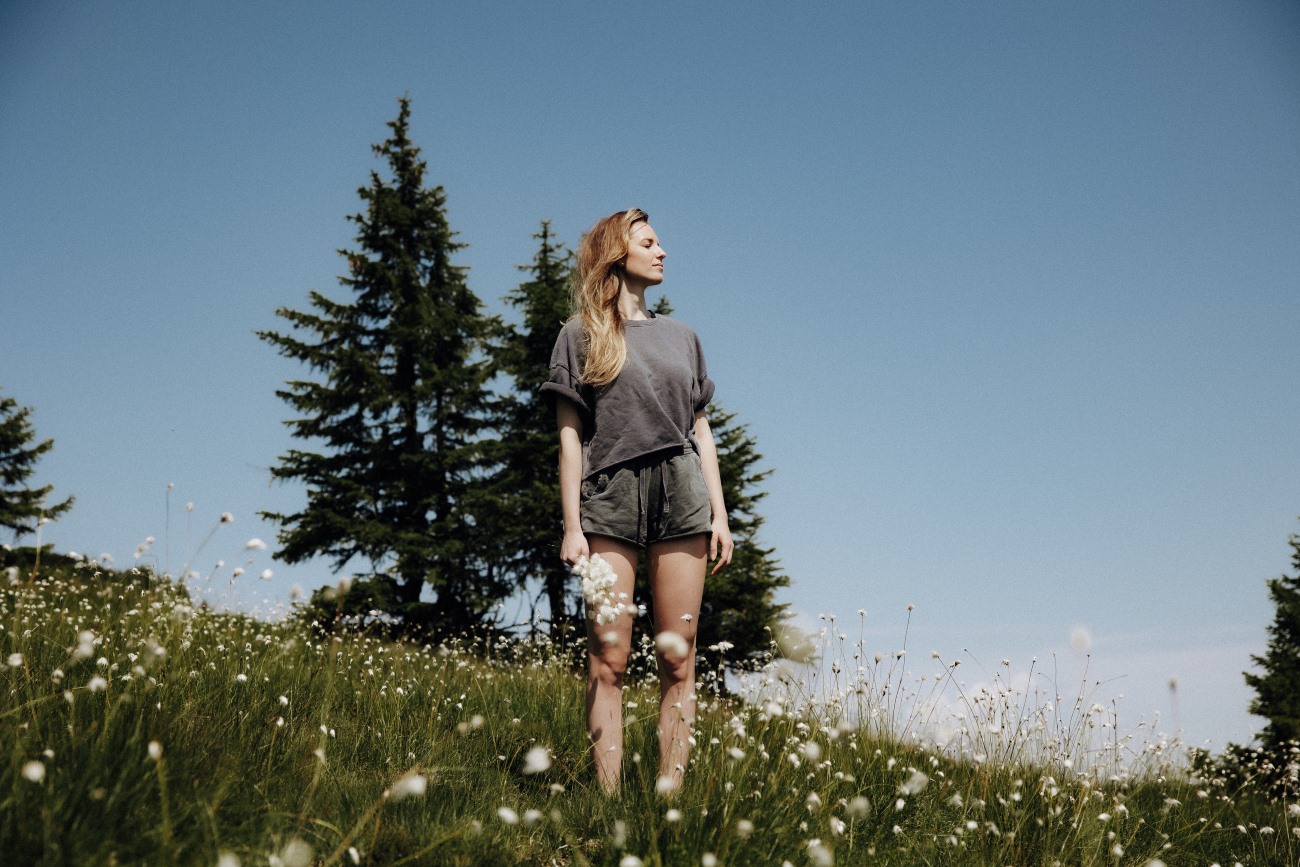 Frau steht auf einer Wiese mit Blumen und blauem Himmel