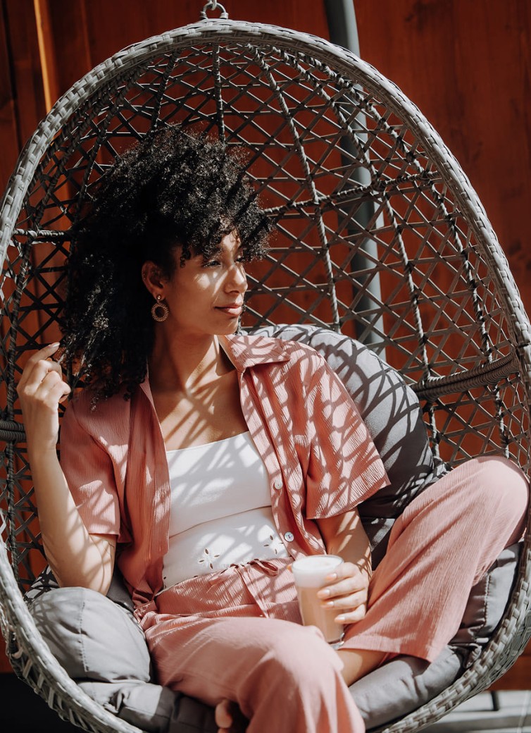 Frau relaxt im gemütlichen Korbsessel und lässt sich die Sonne aufs Gesicht scheinen