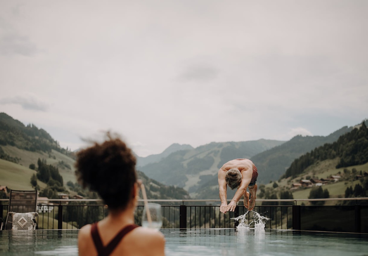 Mann springt in einen Pool mit Berglandschaft im Hintergrund