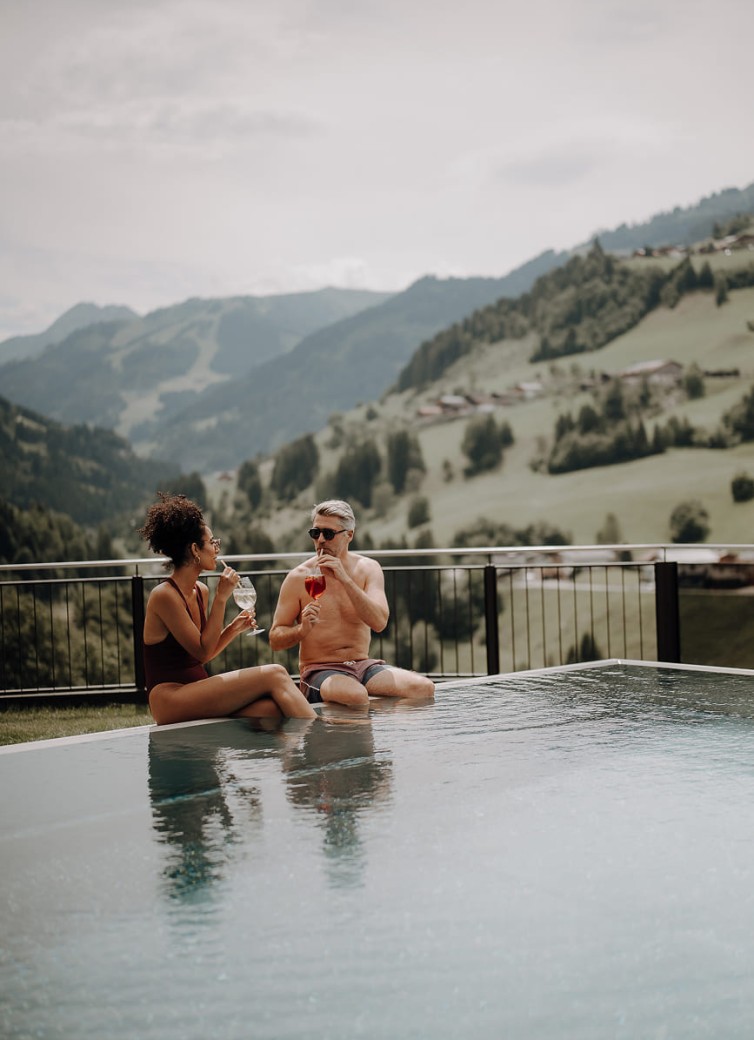 Paar sitzt am Pool mit Bergblick und genießt die Aussicht