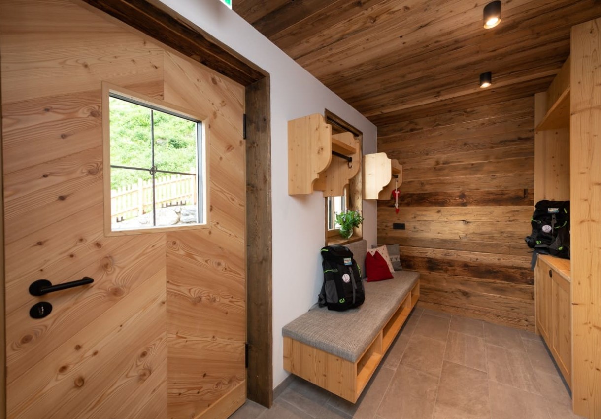 Ein hölzerner Eingangsbereich mit Bank und Rucksäcken auf grauem Boden