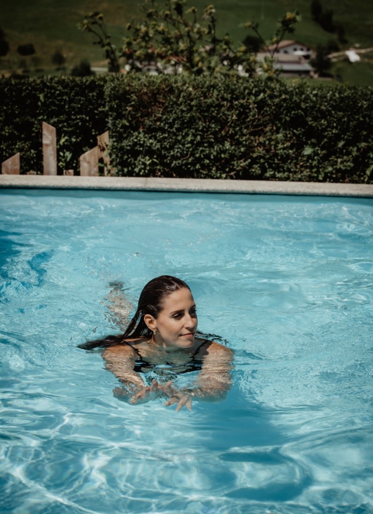Eine Frau schwimmt entspannt in einem Außenpool bei sonnigem Wetter