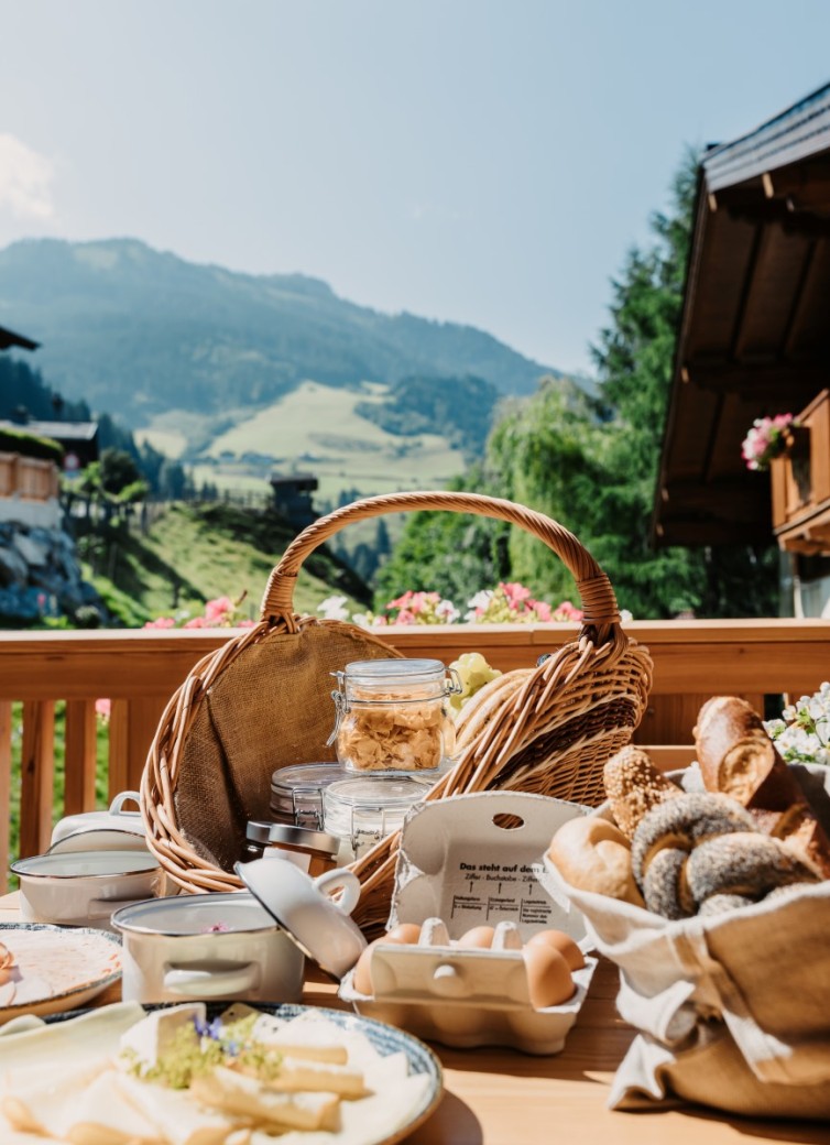 Frühstückskorb auf einem Holztisch mit Aussicht auf alpine Landschaft
