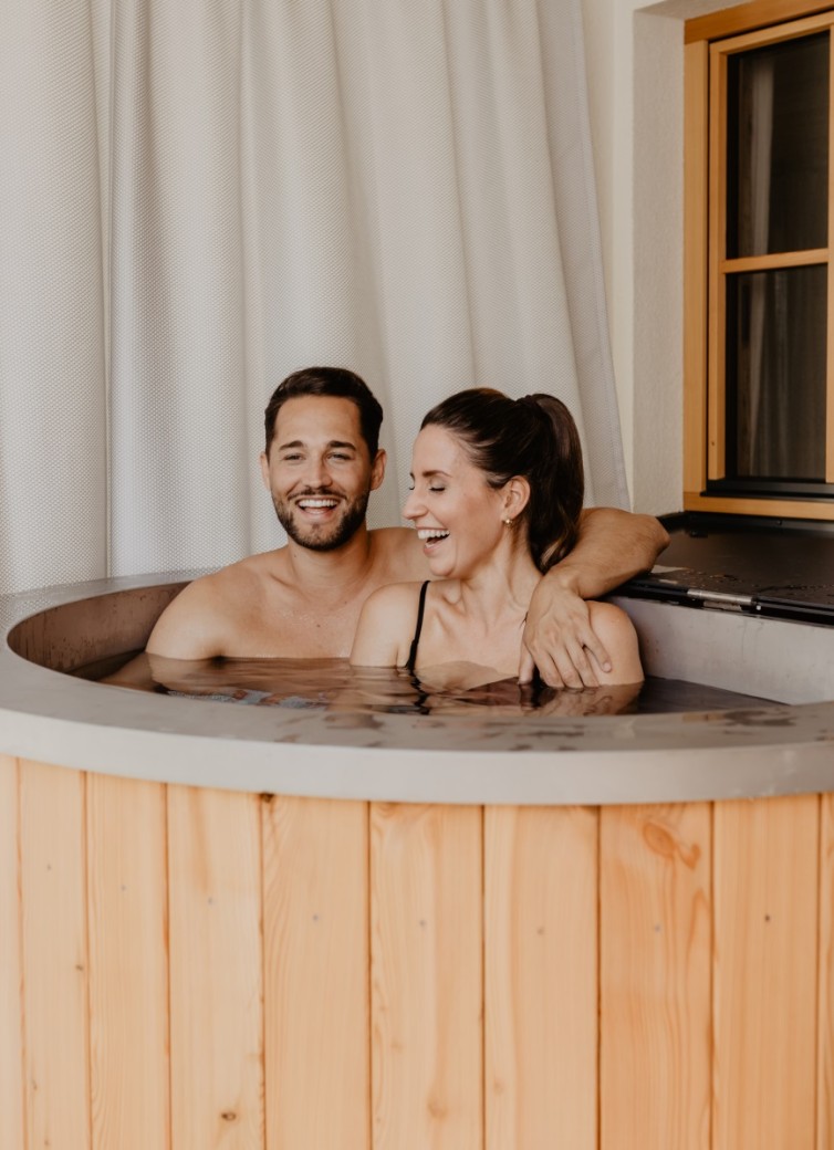 Ein Paar entspannt sich lachend in einem Whirlpool mit Holzverkleidung