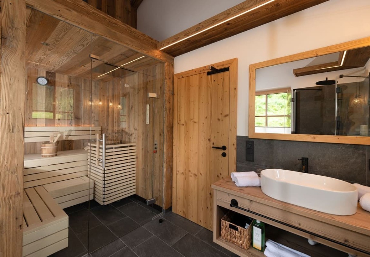 Holzverkleidetes Badezimmer mit Sauna, Waschbecken und großem Spiegel