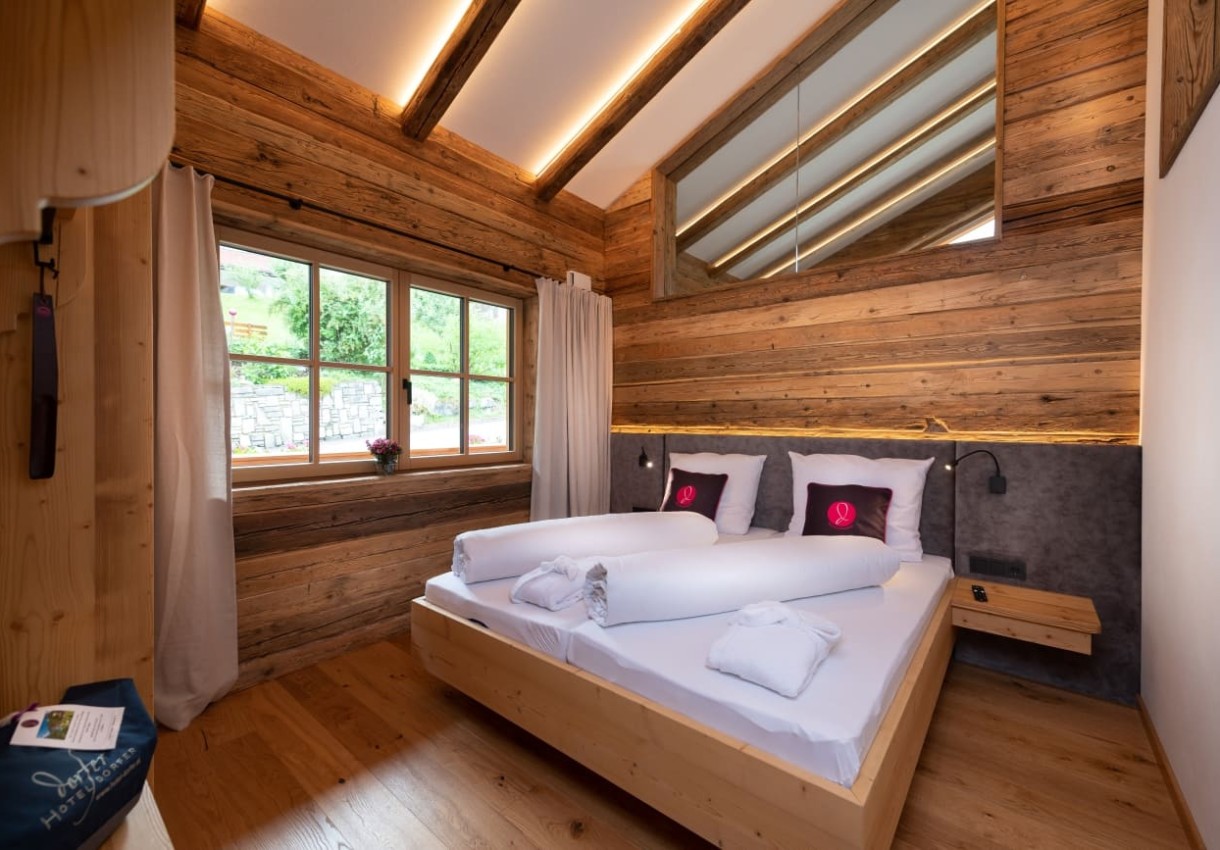 Gemütliches Schlafzimmer mit Holzwänden, großem Bett und Ausblick auf die Natur