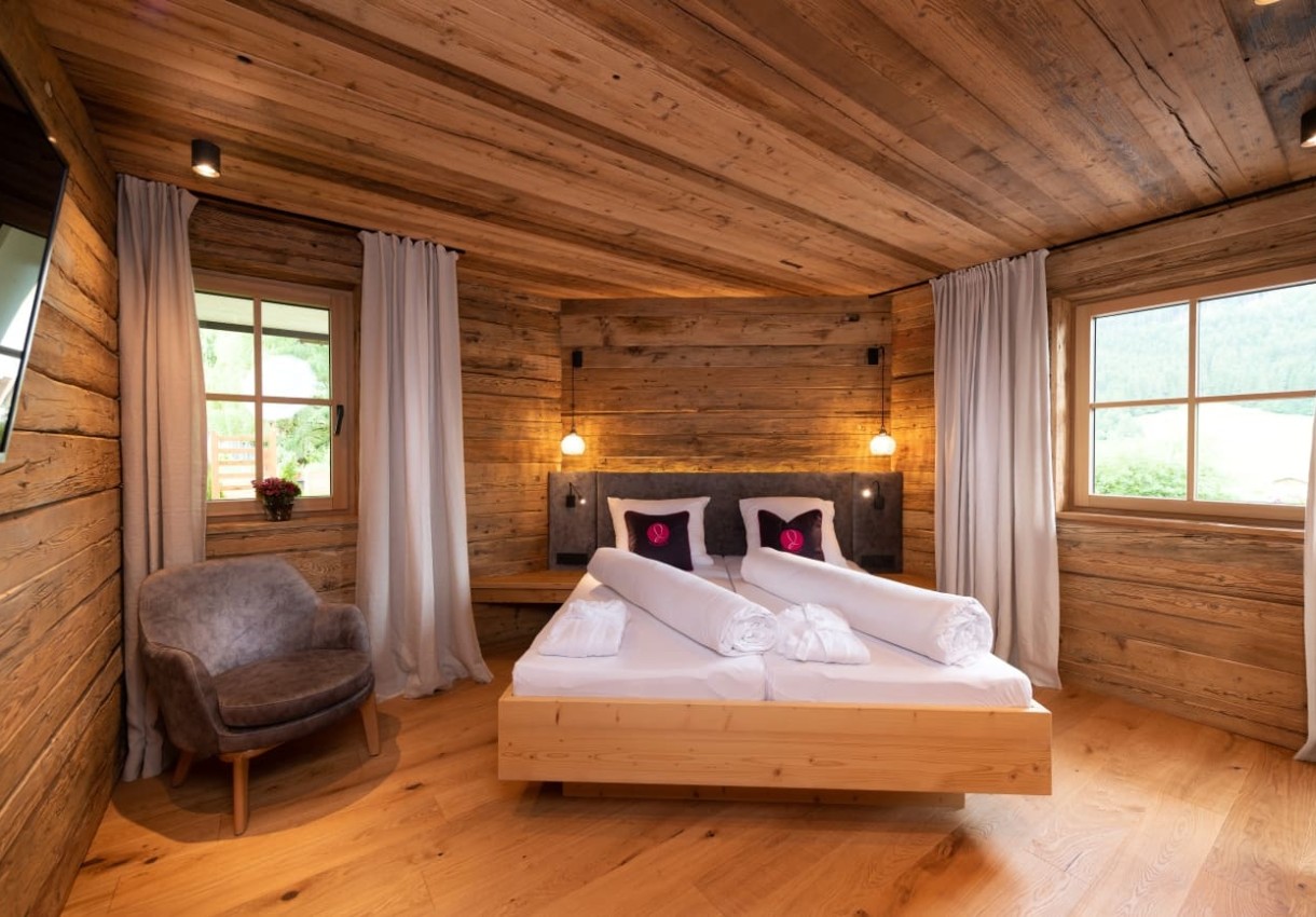 Gemütliches Holzschlafzimmer mit Doppelbett, Sesseln und Fenstern mit Vorhängen