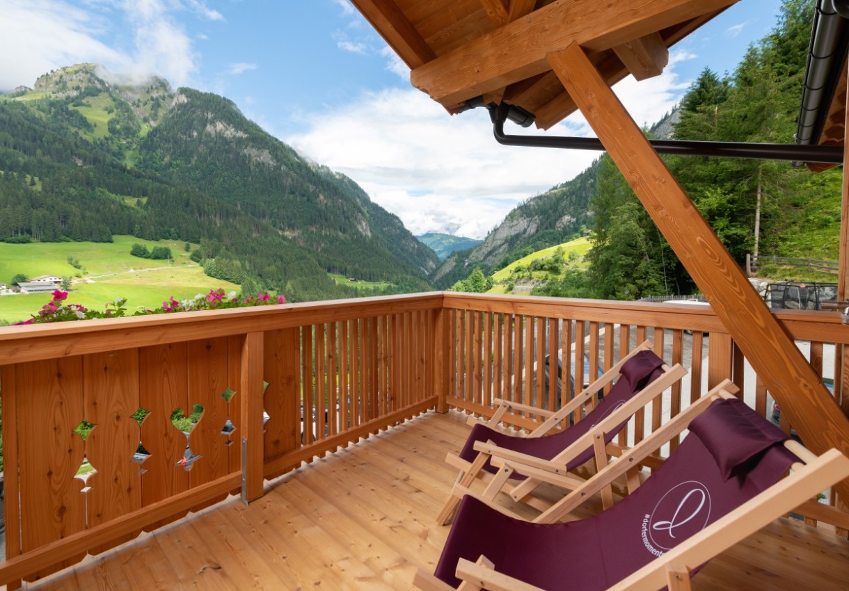 Blick von einem Holz-Balkon auf eine malerische Berglandschaft mit Liegestühlen