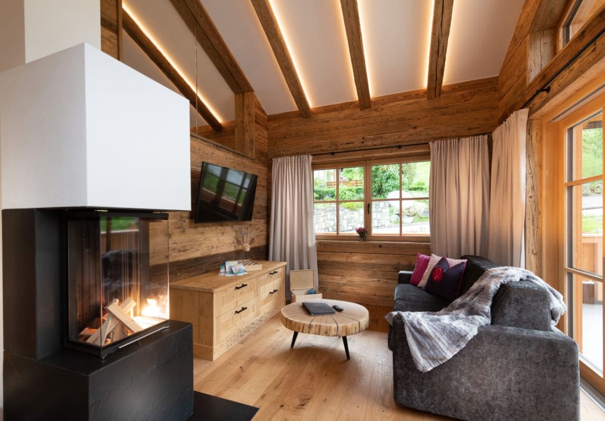 Gemütliches Wohnzimmer mit Kamin, Holzmöbeln und großen Fenstern mit Blick ins Grüne