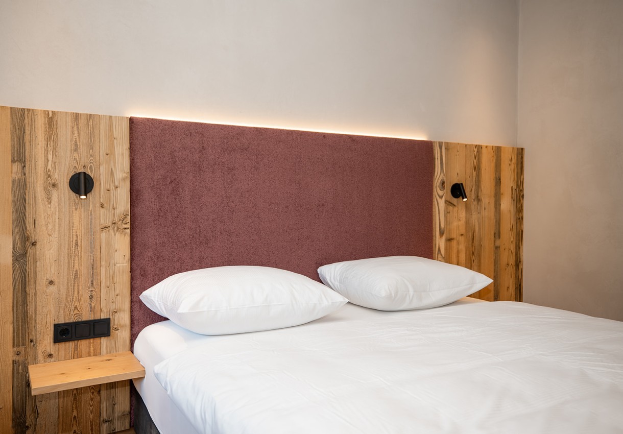 Ein Bett mit Holz- und Stoffkopfteil, weißen Kissen und Bettdecke