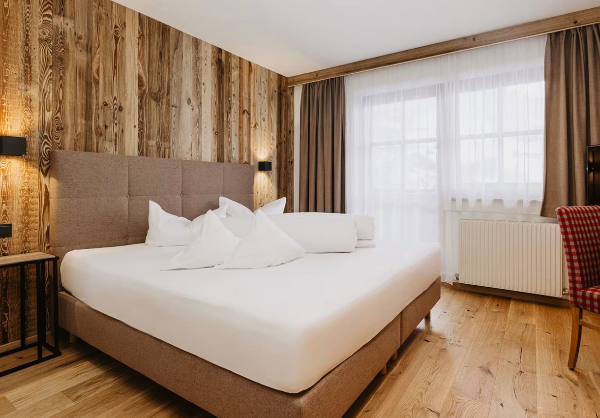 Gemütliches Schlafzimmer mit Holzwänden, großem Bett und großen Fenstern