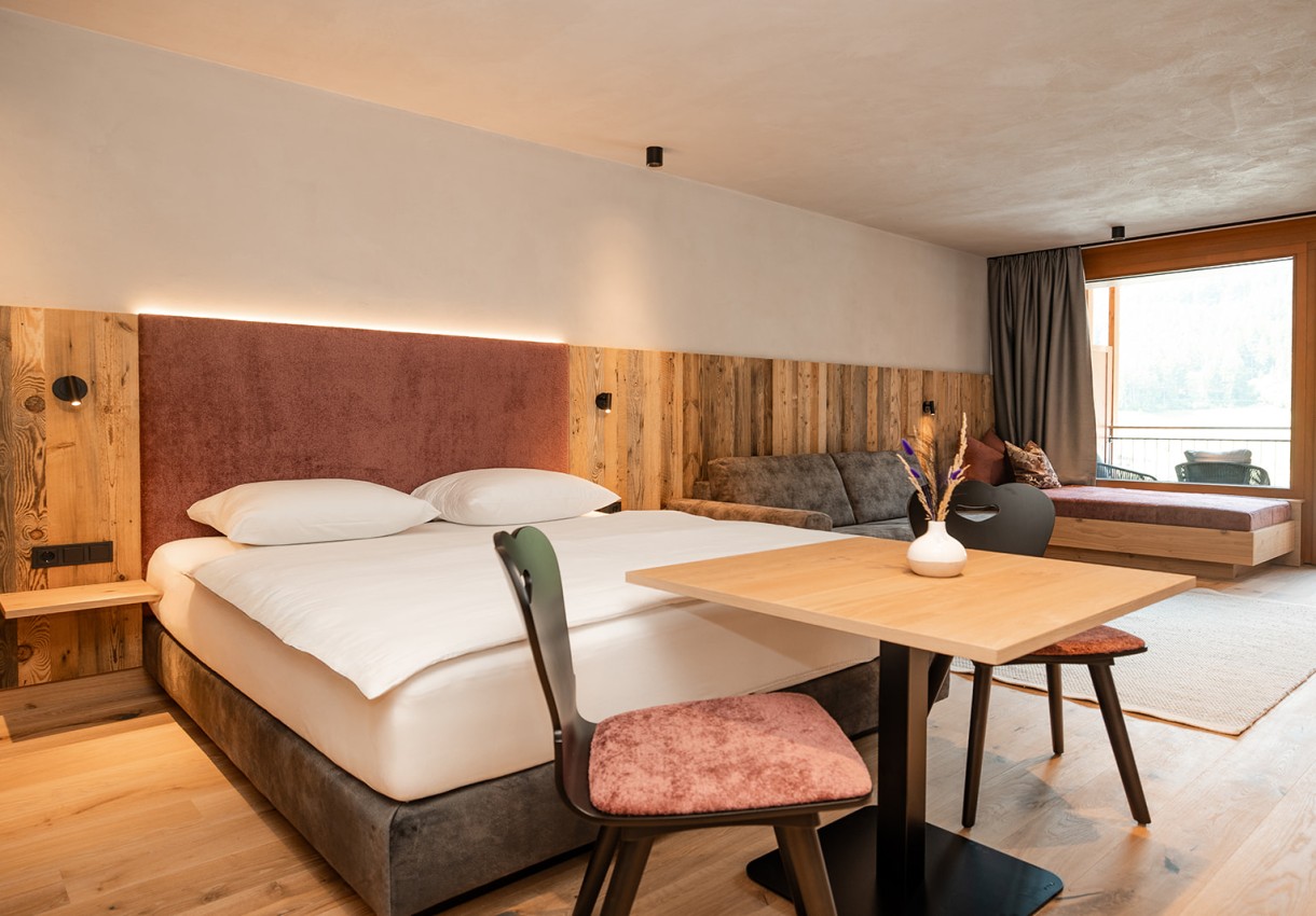 Modernes Hotelzimmer mit Doppelbett, Sofa, Tisch und Stühlen in Holzoptik