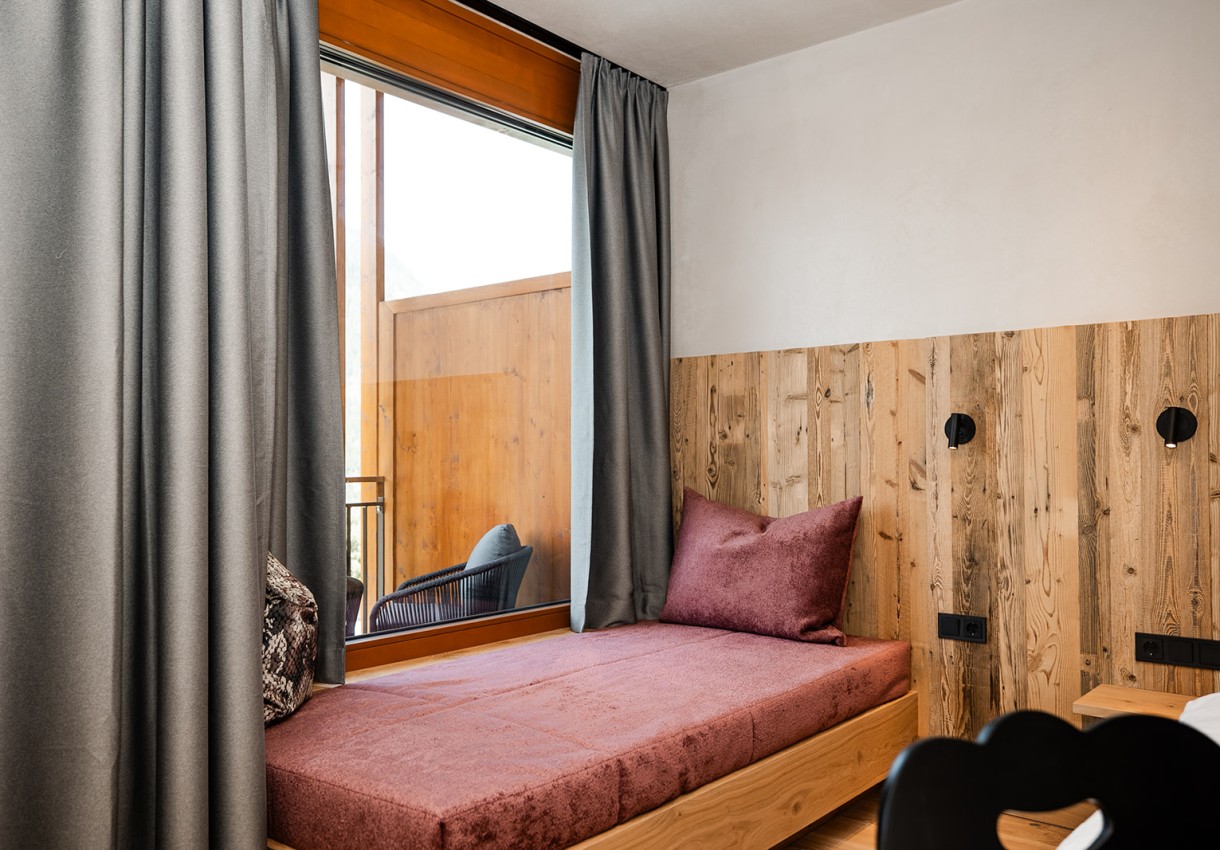 Zimmer mit Holzwand und Tagesbett, das durch ein großes Fenster Licht erhält