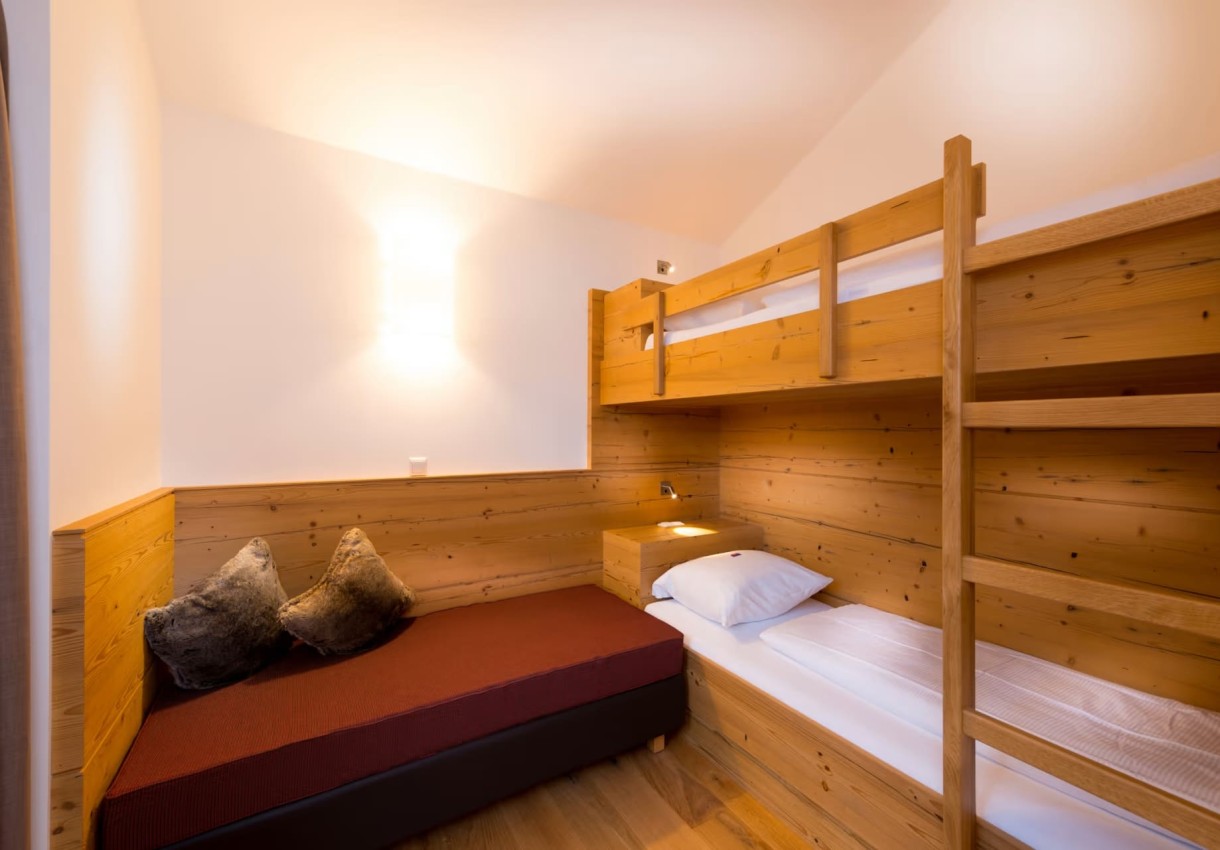 Holzvertäfeltes Zimmer mit Hochbett und Schlafcouch in gemütlichem Licht