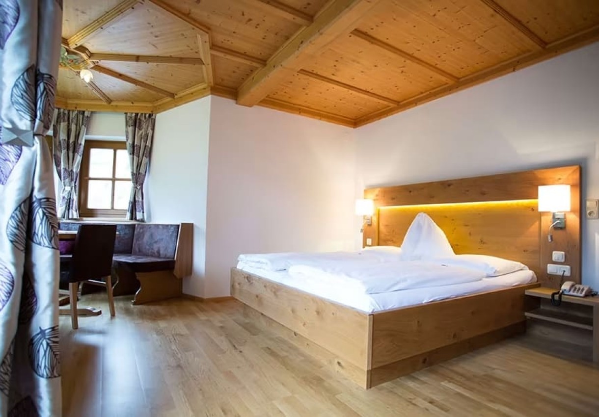 Gemütliches Zimmer mit Holzdecke, Doppelbett, Tisch und Fenster mit Vorhängen